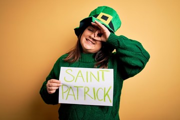 Wall Mural - Plus size woman wearing green hat celebrating st patricks day holding saint patricks day banner with happy face smiling doing ok sign with hand on eye looking through fingers