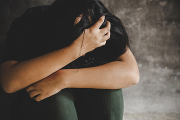 Lonely sad young girl is sitting in the corner crying and holding her head.