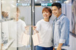 © DragonImages - Happy Asian couple looking at shop windows when choosing shoes in shopping mall