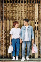 Sticker - Cheerful young couple in love holding shopping-bags and looking at each other