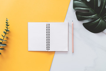 Wall Mural - Tropical green leaf and notebook with pencil on yellow wall and white marble texture abstract background.