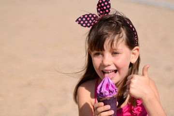 Closeup of pretty little girl eating ice cream outdoors on sunny day. Cute girl in pink swimsuit licking purple ice-cream in waffle cone. Summer, happy childhood concept. Copy space for your text