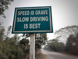 white colour 'speed is grave slow driving is best' text on blue colour rectangular board at the highway