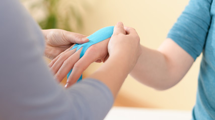 Wall Mural - Female physiotherapist applying kinesio tape on patient's arm. Kinesiology, physical therapy, rehabilitation concept. Cropped shot.