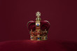 Golden crown on a velvet cushion on a deep red background with copy space