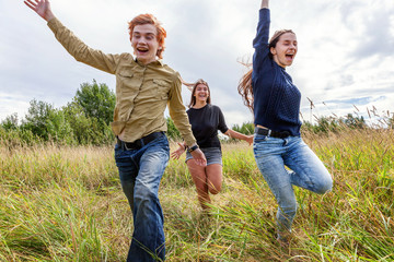 Summer holidays vacation happy people concept. Group of three friends boy and two girls running and having fun together outdoors. Picnic with friends on road trip in nature.