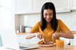 Cheerful young woman using laptop computer have a dinner.