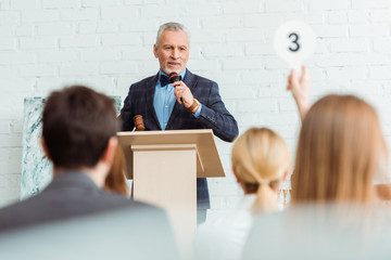 Poster - selective focus of auctioneer talking with microphone and looking at buyer during auction