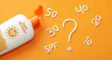 Sunscreen On Orange Background. Plastic Bottle Of Sun Protection And White Cream In The Form Of Question Mark And Numbers SPF. How To Choose A Sunscreen