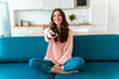© Drobot Dean - Optimistic young woman holding remote control on sofa.