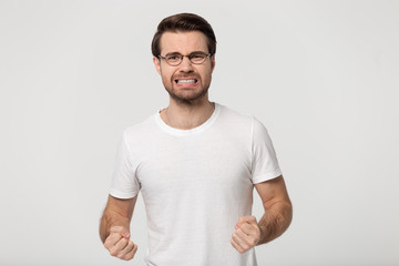 Irritated millennial unhappy guy standing with clenched fists and teeth.