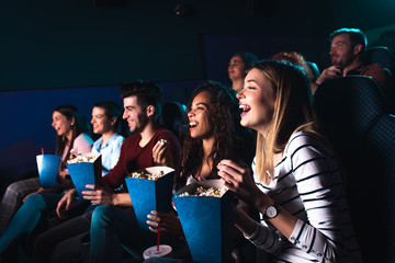 Group of cheerful people laughing while watching movie in cinema.