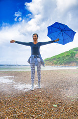 Canvas Print - Woman  holding blue umbrella relaxing at the sea, ocean in background, front view