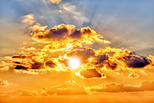 Sunset Sky Landscape Background Natural Color Of Evening Cloudscape With Setting Sun Rays Coming Through Clouds. Orange Clouds Against Blue And Yellow Sky. Colorful Panorama Wallpaper Wide Angle View