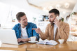 © studioprodakshn - two successful smiling colleagues men working during lunch break at cafe, one pointing at his friend's laptop , common project , multitasking and teamwork concept