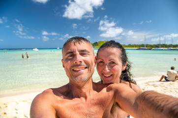 Wall Mural - Happy familty on holiday at the beach. Young couple embracing and taking selfies on the shoreline