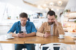 © studioprodakshn - two handsome colleagues men out of office during coffee break at cafe, drinking coffee, checking news in their smartphones , multitasking concept