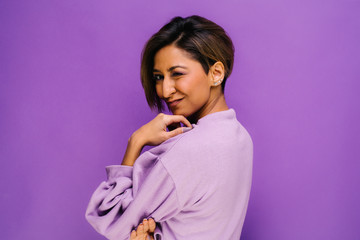 Portrait of young woman with her back to camera and short hair in the studio, with a purple background