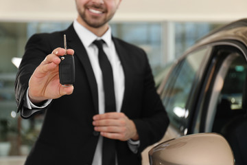 Wall Mural - Young salesman with key near car in dealership, closeup