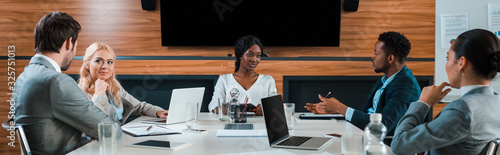 Fotomural panoramic shot of young multicultural businesspeople talking while sitting in co