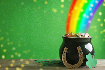 Pot with gold coins, horseshoe and clover leaves on wooden table against green background, space for text. St. Patrick's Day celebration