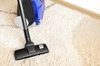 Canister modern vacuum cleaner blue for cleaning the house on the background of a soft beige carpet. Housekeeping, interior, vacuuming. Copy space for text.