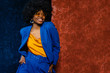 African American fashionable woman wearing yellow sunglasses, top, classic blue suit. Young beautiful happy smiling model posing near colorful walls. Fashion portrait. Copy, empty space for text