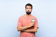 © luismolinero - Young man with beard holding a take away coffee over isolated blue background with sad and depressed expression