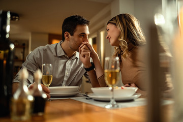 Young romantic man kissing girlfriend's hand during dinner at dining table.