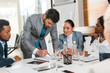 © LIGHTFIELD STUDIOS - selective focus of handsome businessman holding pencil while standing near multicultural colleagues sitting at desk in conference hall