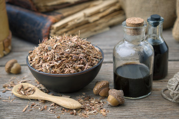 Wall Mural - healthy oak bark in black ceramic bowl, infusion bottle and old books on table. herbal medicine.