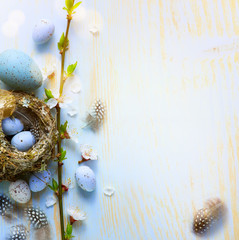 Holiday Easter banner or greeting card background; Spring tree flowers and Easter eggs in birds nest on sunny light  wooden background