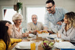 © Drazen - Happy mid adult man serving lunch to his family at dining table.