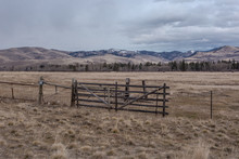 Vintage Wooden Fencing In An Open Field With Tree Line And Mountain Range On Overcast Day