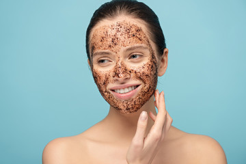 Wall Mural - beautiful smiling woman applying coffee scrub on face, isolated on blue