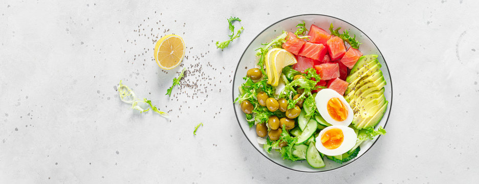 Ketogenic, keto or paleo diet lunch bowl with salted salmon fish, lemon, avocado, olives, boiled egg, cucumber, green lettuce salad and chia seeds. Healthy food trend. Top view. Banner