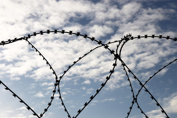 Silhouette of barbed wire on background of blue sky and white clouds. Concept of boundary, prison or war