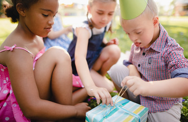 Down syndrome child with friends on birthday party outdoors, opening presents.