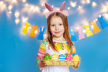 Happy easter! funny child girl with bunny ears and eggs on a blue background