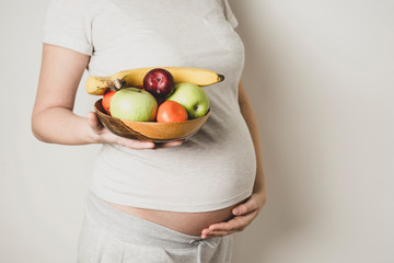 Pregnant belly, woman with healthy food, bowl of fruits in hands. Copy space.