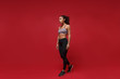 © ViDi Studio - Attractive young african american sports fitness woman in sportswear posing working out isolated on red wall background, studio portrait. Sport exercises healthy lifestyle concept. Looking aside.