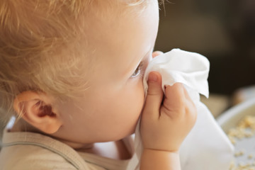 child wipes his nose with white handkerchief. sick child eats sitting on feeding chair. Kid with cold rhinitis. virus and infection. Coronavirus symptom