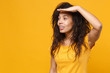 © ViDi Studio - Smiling young african american woman girl in casual t-shirt posing isolated on yellow orange background. People lifestyle concept. Mock up copy space. Hold hand at forehead looking far away distance.