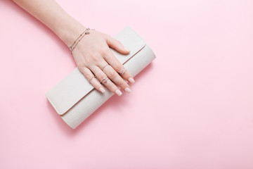 Female hand with jewelry and clutch bag on pink background