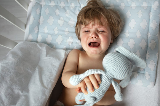 Baby crying in the bed before a bedtime. Child want to sleep. Toddler emotion before a sleeping. View from above.