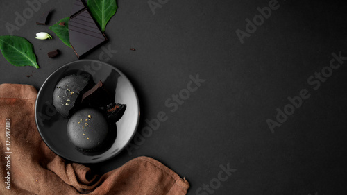 Top view of dark chocolate macarons on black plate on dark table Tableau sur Toile