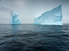 Two Icebergs In Dark Water In Antarctica