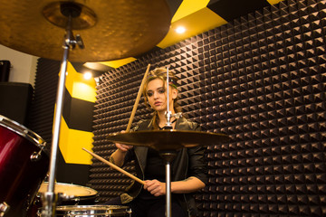 young beautiful tattooed girl in a leather jacket plays drums in a recording Studio on the bright black and yellow band