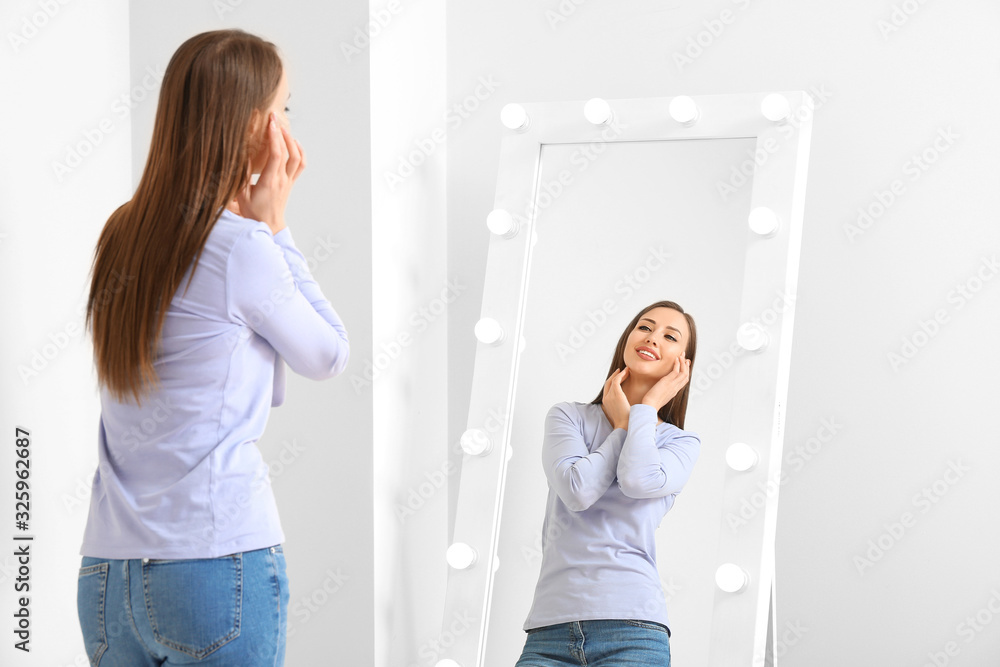 Beautiful young woman looking in mirror at home