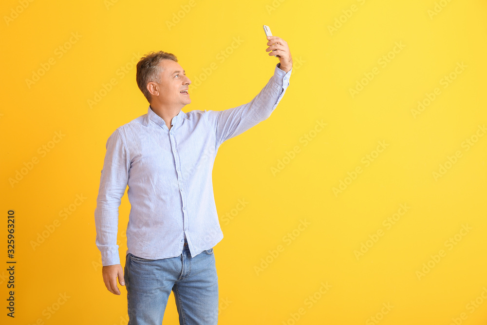 Mature man taking selfie on color background